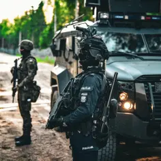 Służba mundurowa w akcji. Policjanci w pełnym rynsztunku, obok opancerzonego pojazdu, czuwają.