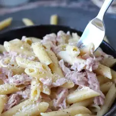 Penne z kremowym sosem i kawałkami szynki parmeńskiej, posypane parmezanem i pieprzem. Widok z bliska na apetyczne danie.