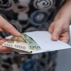 Dłonie trzymają kopertę z polskimi banknotami. Kto może otrzymać rentę wdowią?