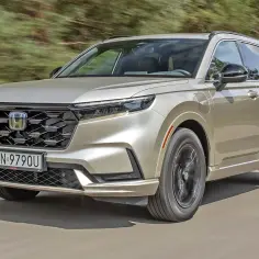 Złoty Honda CR-V Hybrid w ruchu, z widocznym grillem i światłami LED.