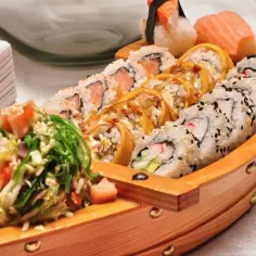 Drewniana łódka pełna sushi, przypominająca o tradycji, skąd pochodzi sushi. Różnorodne rolki i nigiri kuszą smakiem.