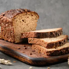 Kromka chleba proteinowego z ziarnami, obok szklanka mleka i kłosy zboża.