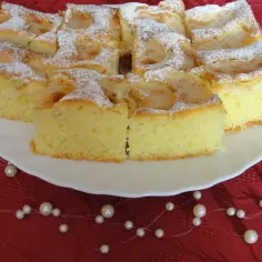 Puszyste ciasto z owocami na oleju i kruszonką, posypane cukrem pudrem, prezentuje się apetycznie na białym talerzu.