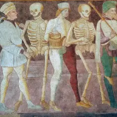 Szkielety i ludzie w średniowiecznych strojach idą w pochodzie. To mroczny obraz danse macabre, przypominający o nieuchronności śmierci.