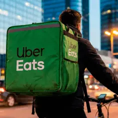 Kurier Uber Eats na rowerze z zieloną torbą na tle miejskiego krajobrazu.
