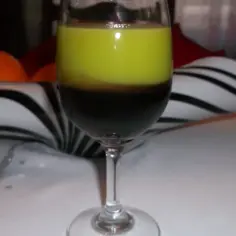 Dwukolorowy drink z wiśniówką, gdzie ciemny płyn kontrastuje z jasnozieloną warstwą. Na tle widać pomarańcze i ozdobną misę.