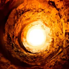 Wnętrze skalnego tunelu, przypominającego najgłębszy odwiert, rozświetlone jasnym światłem u wylotu.