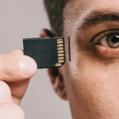 Zbliżenie na oko i dłoń trzymającą kartę pamięci, sugerujące futurystyczny **efekt mandeli** i integrację technologii z człowiekiem.