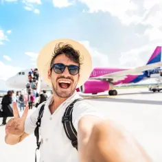 Szczęśliwy turysta z plecakiem i kapeluszem robi selfie na tle samolotu. Czas na przygodę, co po turystyce i rekreacji?
