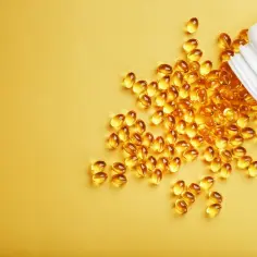 Żółte kapsułki ibuvit rozsypane z białego opakowania na żółtym tle.