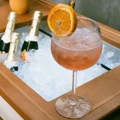Aperol Spritz z pomarańczą i butelkami prosecco w lodzie. Brak bąbelków w drinku może świadczyć o objawy niskiej zawartości gazu w prosecco.