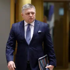 Robert Fico, prezydent Słowacji, w eleganckim garniturze idzie korytarzem, trzymając teczkę z dokumentami.