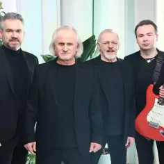 Czterech mężczyzn w czarnych strojach, jeden z nich trzyma czerwone gitary.