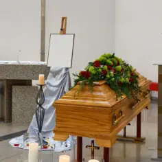 Drewniana trumna z kwiatami, świece i krzyż w kościele. Zastanawiasz się, ile zarabia żałobnik?