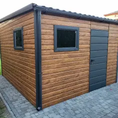 Nowy domek narzędziowy DIY z drewnopodobnym wykończeniem, dwoma oknami i szarą drzwiami, stoi na kostce brukowej.