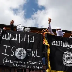 Osoby z zasłoniętymi twarzami trzymają czarne flagi z napisami w języku arabskim i angielskim, w tym "Islamic State of Jammu Kashmir & Ladakh".