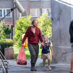 Mężczyzna z dziewczynką idą ulicą, za nimi widać ekipę filmową i mikrofon.