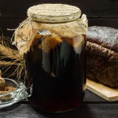 Słoik z domowym kwasem chlebowym, bochenek chleba żytniego, miseczka z mąką i kłosy zboża.