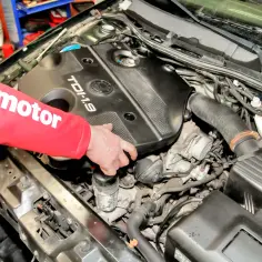 Ręka w czerwonej bluzie z napisem "motor" pokazuje silnik TDI 1.9. Gdzie jest termostat w Golfie 5 1.9 TDI?