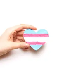 Dłoń trzyma serce z flagą transpłciową. Symbol dumy i akceptacji dla każdej osoby transpłciowej.