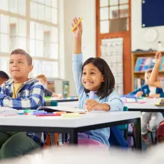 Dzieci na lekcji, jedna dziewczynka podnosi rękę, zastanawiając się, kiedy złożyć wniosek o wydłużenie etapu edukacyjnego.