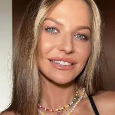Kobieta z niebieskimi oczami i blond włosami z pasemkami, które przypominają "money piece". Uśmiecha się, nosząc kolorowy naszyjnik.