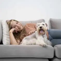 Uśmiechnięta dziewczyna leży na kanapie obok białego psa.