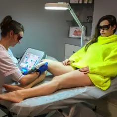 Specjalistka wykonuje depilację laserową nogi klientki. Czy depilacja laserowa boli? Zależy od indywidualnego progu bólu.