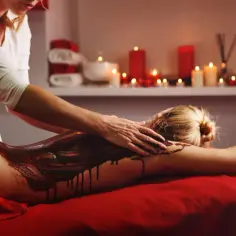 Relaksacyjny masaż gorącą czekoladą. Ciemna, płynna czekolada spływa po plecach kobiety, podczas gdy masażystka delikatnie ją rozprowadza.