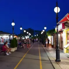 Wieczorna atmosfera na promenadzie w Złotych Piaskach. Ludzie spacerują, sklepy są otwarte, a latarnie rzucają ciepłe światło.