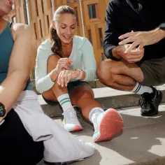Trzy osoby w strojach sportowych odpoczywają po marszobiegu, sprawdzając wyniki na zegarkach.