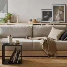 Jak ożywić beżowy salon? Dodaj rośliny, kosze z plecionki i ciekawe tekstylia. Wygodna sofa, stolik i regał pełen książek tworzą przytulną przestrzeń.