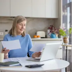 Kobieta po 50. roku życia analizuje dokumenty przy laptopie, być może w kontekście ubiegania się o rentę chorobową.