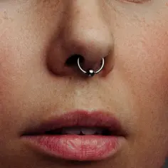 Zbliżenie na twarz z piegami i kolczykiem w nosie. Czy septum zarasta? Delikatny błysk na metalowej kuli.