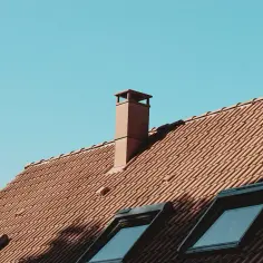 Brązowy, ceglany dach z kilkoma oknami połaciowymi i kominem. Nawet po deszczu, mokry komin na strychu nadal stoi dumnie.