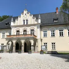 Elegancki dwór w Łodygowicach z arkadowym podcieniem i ozdobną balustradą, otoczony brukowanym dziedzińcem.