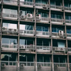 Szare okna i balkony z klimatyzatorami na betonowej fasadzie. Czy balkon wlicza się do metrażu?