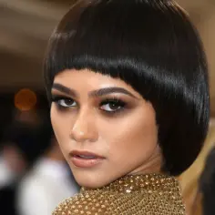Zendaya w odważnej fryzurze na pazia, z błyszczącym złotym kołnierzem, emanuje pewnością siebie.