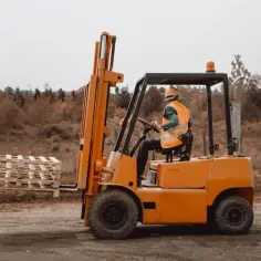 Operator wózka widłowego w kamizelce odblaskowej przewozi palety. Zastanawiasz się, ile zarabia operator wózka widłowego?