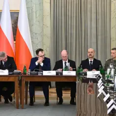 Uczestnicy obrad Rady Bezpieczeństwa Narodowego siedzą przy stole, za nimi polskie flagi.