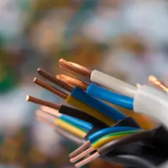 Przewody elektryczne z odsłoniętymi miedzianymi żyłami, w izolacjach w różnych kolorach faz: białym, niebieskim, żółtym i brązowym.