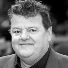 Uśmiechnięty Robbie Coltrane, aktor znany z roli Hagrida, w czarno-białym portrecie.
