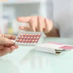 Dłoń trzyma blister tabletek antykoncepcyjnych. Farmaceuta wyjaśnia możliwe qlaira skutki uboczne.