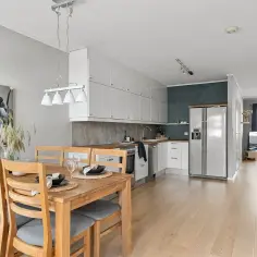 Jasny salon z jadalnią i kuchnią. Drewniany stół z krzesłami, białe szafki kuchenne, lodówka. Idealne miejsce na rynku wtórnym.