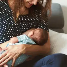 Mama karmi piersią dziecko na kanapie. To piękny czas podczas urlopu rodzicielskiego, pełen bliskości i miłości.