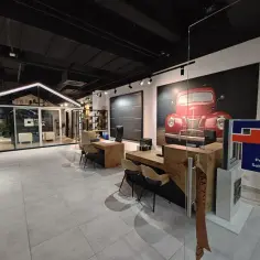 Nowoczesny salon okien i drzwi z ekspozycją, grafiką czerwonego auta i ladą sprzedażową.