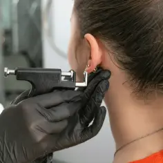 Osoba w czarnej rękawiczce zakłada kolczyk leczniczy do ucha za pomocą pistoletu.