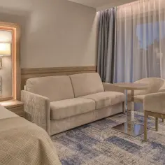 Przytulny pokój w hotelu 5 gwiazdkowym nad morzem. Kanapa, fotele, stolik i łóżko tworzą komfortową przestrzeń.
