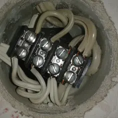 Widok z góry na puszkę instalacyjną z połączonymi kablami. Widać kostkę elektryczną z sześcioma śrubami, do której podłączone są białe przewody.