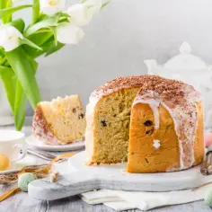 Pyszna babka włoska z lukrem i czekoladą, udekorowana na Wielkanoc. Obok filiżanki, tulipany i kolorowe jajka.